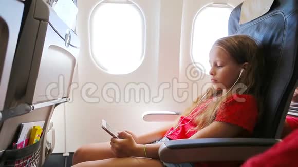 可爱的小女孩坐在靠窗的飞机上小孩在附近听音乐和发送信息视频的预览图