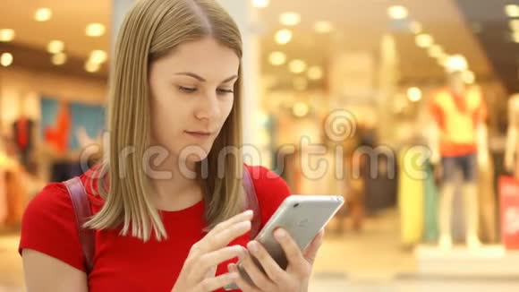 年轻漂亮的女人坐在购物中心微笑用她的智能手机和朋友聊天视频的预览图