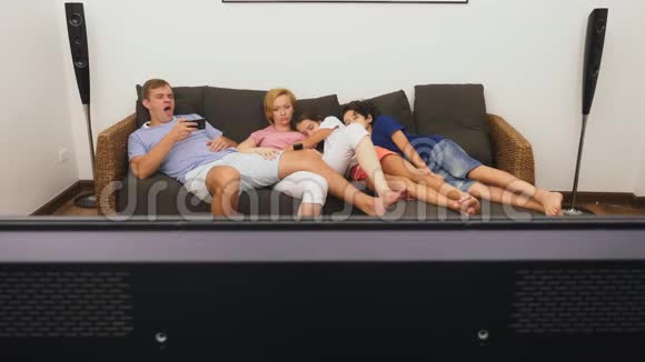 可爱的家人妈妈爸爸女儿和儿子一起在客厅里看电视在前面睡着了视频的预览图