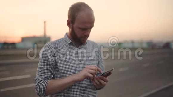 一个年轻人在日落或日出时在街上使用他的智能手机视频的预览图