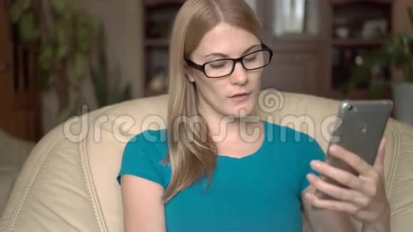 聪明的戴眼镜的休闲女人坐在家里的椅子上用信用卡在线购买智能手机视频的预览图