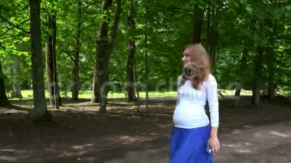 带帽子和电话的漂亮孕妇在公园散步视频的预览图
