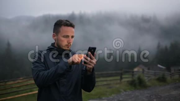 一个年轻人晚上在山里用电话在雾中的森林周围视频的预览图