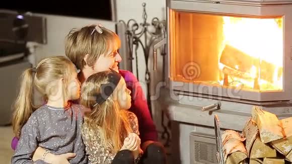 圣诞前夜祖母和她的两个小孙女坐在家里的壁炉旁视频的预览图