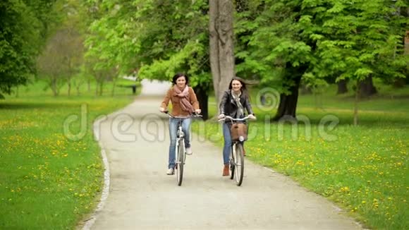 笑两个女朋友在公园骑自行车年轻有趣的女人与自行车一起度过时光视频的预览图
