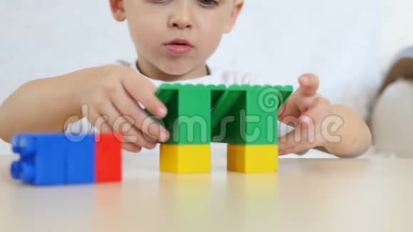 一个孩子正在玩彩色积木坐在白色背景上的桌子上慢动作孩子和玩具特写视频的预览图