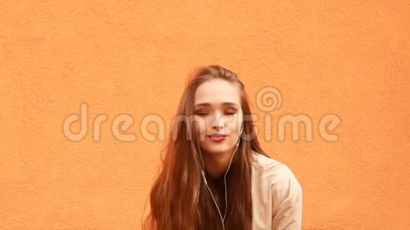 戴着耳机的滑稽卷发女孩微笑着在橙色背景下接吻视频的预览图