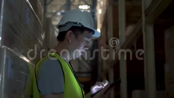 年轻的仓库工人戴着安全安全帽正在仓库用数码平板电脑检查订单细节视频的预览图