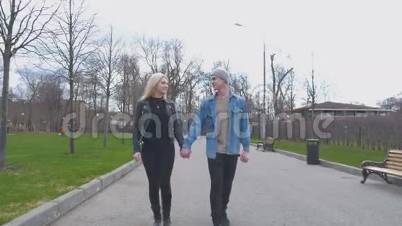 年轻漂亮的一对金发女郎和她的男朋友正牵着手在公园里散步去看摄像机一个美丽的视频的预览图
