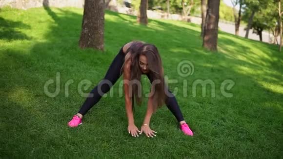 灵活的年轻女孩在公园的草地上伸展经过在绿色城市公园的长时间充满挑战的跑步训练视频的预览图