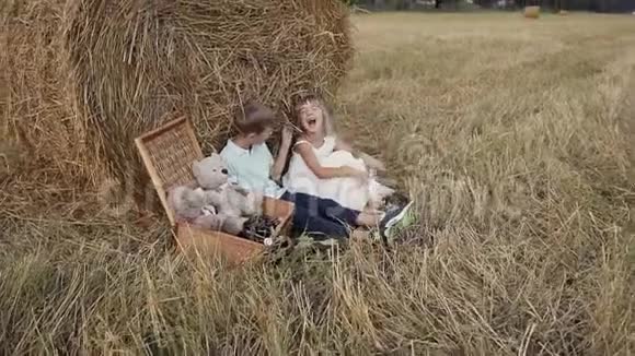 一个小女孩对男孩笑得很开心女孩和男孩带着草捆在田野里散步日落视频的预览图