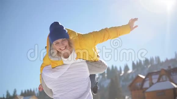 强壮的男孩带着女友在他的肩膀上并在蓝天背景上旋转她快乐的夫妻玩冬天视频的预览图
