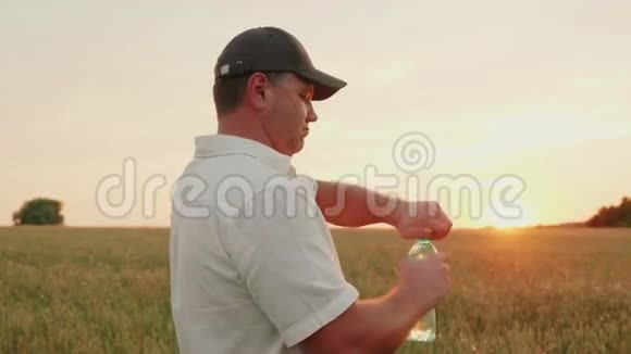 一个中年农民打开一瓶水和饮料日落时分站在麦田里视频的预览图