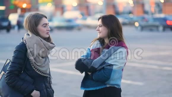 两个年轻漂亮的学生时髦的女孩在汽车附近的城市街道上谈笑风生稳重的凸轮缓慢的视频的预览图