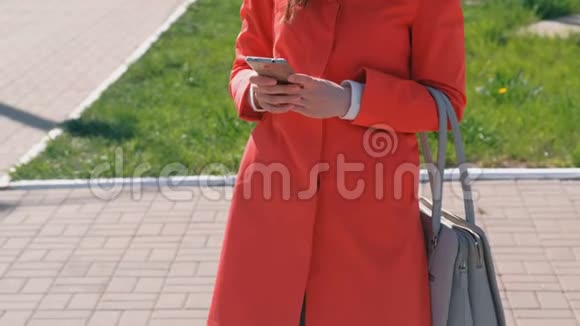 不可辨认的穿着红色外套的女人等着某人检查她的手机发短信特写双手视频的预览图