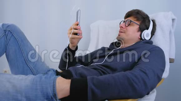 人类在智能手机上用耳机听音乐用卡拉OK唱一首歌在扶手椅上放松时间视频的预览图