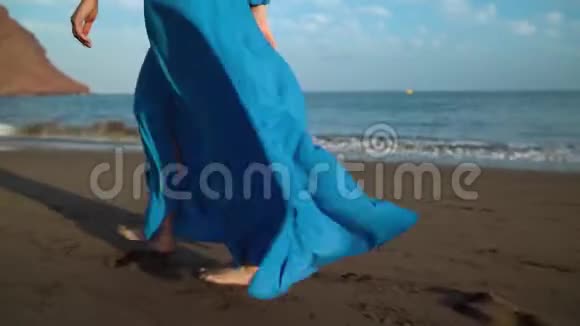 一个穿着漂亮蓝色裙子的女人在黑色火山海滩上行走的腿视频的预览图