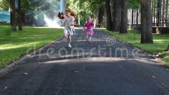 两个快乐的小女孩在绿色的夏日公园里用风车奔跑视频的预览图
