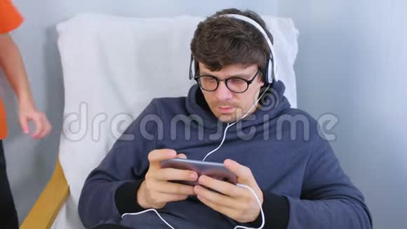 戴着眼镜和耳机的男人和他的儿子在智能手机里玩游戏玩家放松视频的预览图