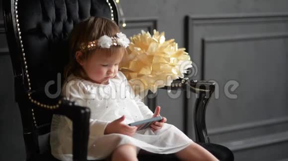 可爱的女婴玩智能手机孩子穿着漂亮的裙子用电话圣诞快乐视频的预览图