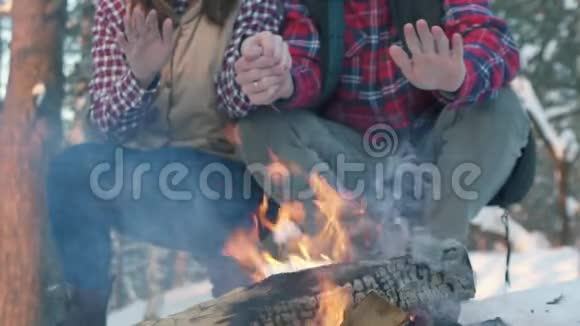一对年轻人穿着冬天的衣服在树林里温暖他们的手在火边一次冬季野餐视频的预览图