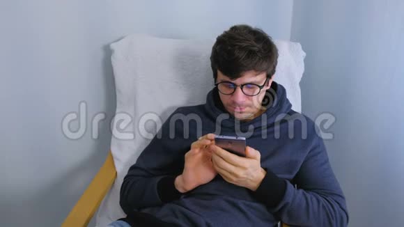 戴眼镜的人正坐在扶手椅上的智能手机上在社交媒体上键入一条信息视频的预览图