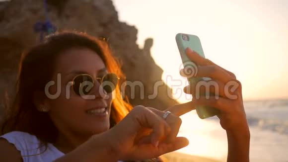 美丽的年轻混合种族女孩拍摄自拍照片同时放松在海滩上的吊床惊人的日落高清高清视频的预览图