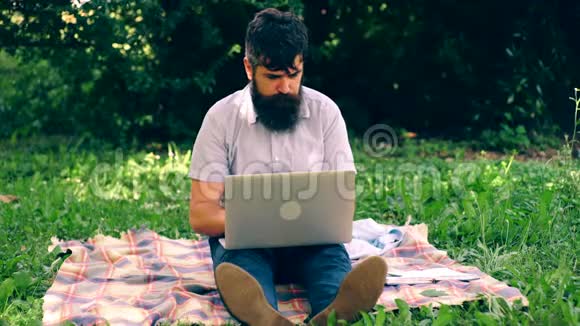 一个留胡子的人在公园里拿着笔记本电脑视频的预览图
