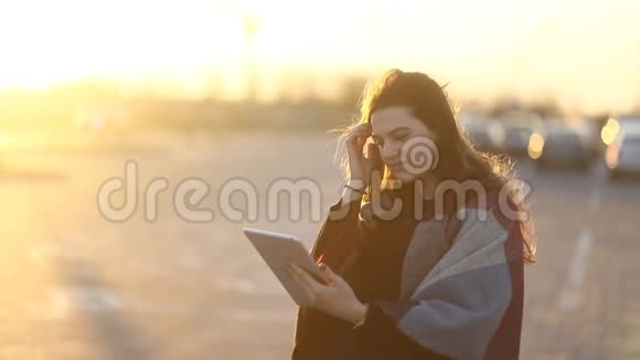 美丽的年轻女子使用平板电脑在户外的街道上日落阳光明媚慢稳定视频的预览图