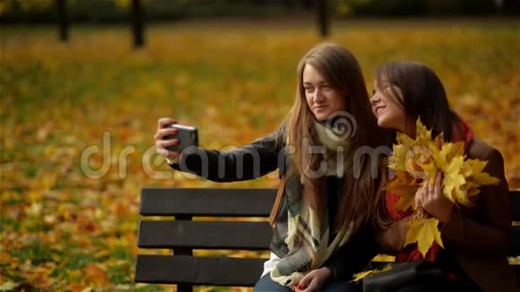 漂亮的女孩让自拍在长凳上的智能手机两位年轻女性喜欢户外活动和与自拍视频的预览图