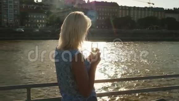 在多瑙河上巡航一个女人拿着一杯香槟在船上的帆在河堤的背景下视频的预览图