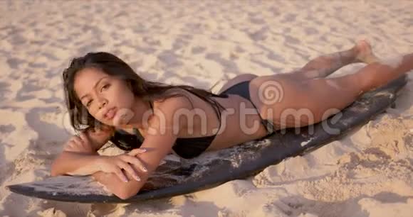女人躺在冲浪板上在沙滩上晒日光浴视频的预览图