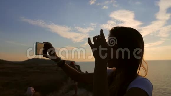 年轻的混血女孩在美丽的日落背景下使用手机自拍照片高清慢镜头视频的预览图