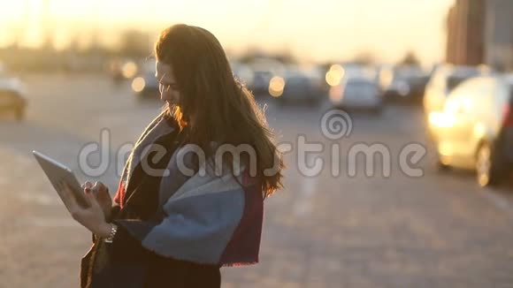 带着围巾的年轻微笑的女人在停车场的户外使用平板电脑奇妙的日落慢节奏视频的预览图