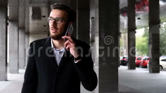 一位穿着经典西装外套英俊的年轻商人正在商业区大街上用智能手机聊天视频的预览图