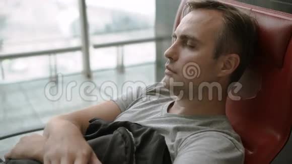 英俊疲惫的年轻人睡在机场航站楼长途连接飞行时差视频的预览图