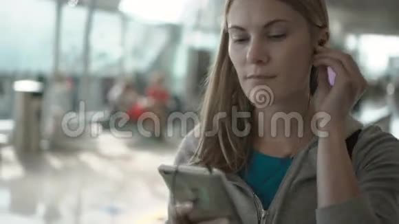 在机场候机楼里用牵引器放松的女人利用她的智能手机听音乐视频的预览图