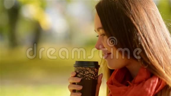 秋天女孩喝咖啡秋季概念年轻女性在秋季公园享用一次性咖啡杯热饮视频的预览图