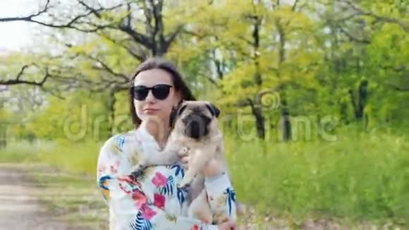 带着你最喜欢的小狗在公园里散步年轻的女人拿着一壶甜饼走在春天的森林里视频的预览图