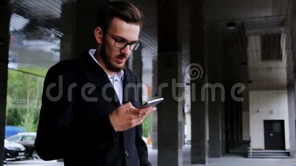 一位年轻的成功经理穿着经典的西装和外套站在他办公室旁边的街道上记录声音视频的预览图