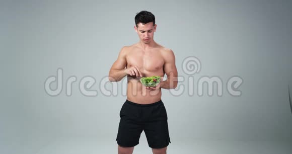 一个男性健身模特拿着塑料碗在白色背景上吃新鲜沙拉他微笑着为了健康的生活视频的预览图
