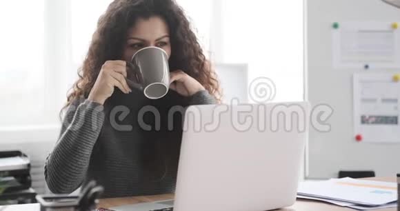 女商人喝咖啡工作在办公室笔记本电脑上视频的预览图