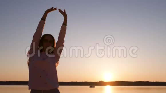 年轻女子在春天的河滩黄金时段享受日落穿着白色的裤子短汗和夹克视频的预览图