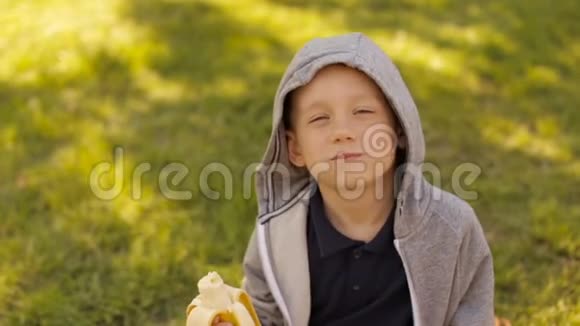 一个男孩正在夏天的公园里吃一根新鲜的香蕉视频的预览图