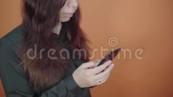年轻的女人手拿手机在橙色的背景上女性在智能手机上输入信息视频的预览图