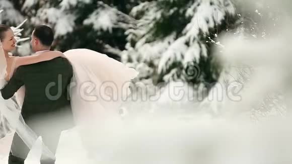 新郎在雪地里旋转着快乐的新娘手里握着她在雪地里旋转着冷杉林视频的预览图