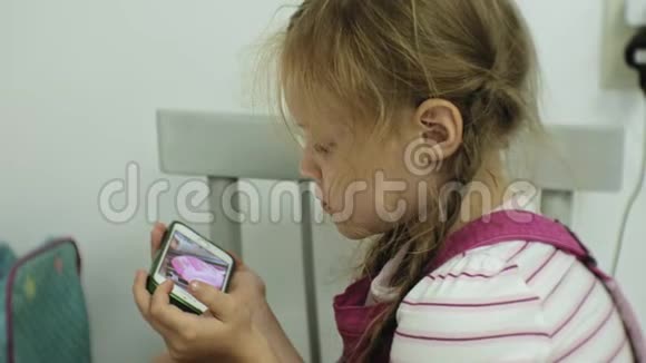 坐在椅子上的小女孩试图用她的智能手机玩游戏儿童使用手机视频的预览图