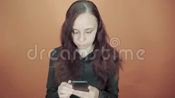 年轻的女人手拿手机在橙色的背景上女性在智能手机上输入信息视频的预览图