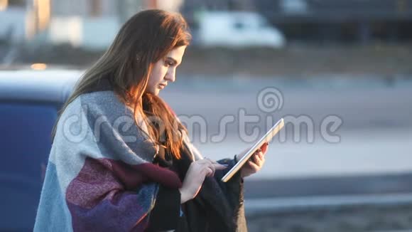 年轻女孩在汽车附近的街道上用平板电脑在户外按摩慢稳定视频的预览图