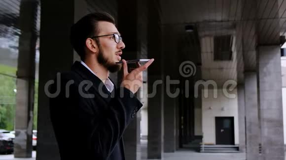 一位年轻成功的律师穿着经典的西装和外套站在他办公室旁边的街道上记录声音视频的预览图